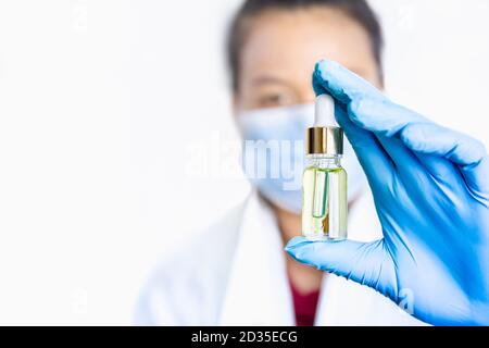 Main dans des gants médicaux bleus tenant une goutte d'huile de cannabis CBD. Banque D'Images