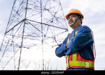 Les ingénieurs asiatiques portent des vêtements de sécurité et adoptent la tablette en toute confiance dans la qualité de l'énergie électrique sur la tour haute tension, Banque D'Images