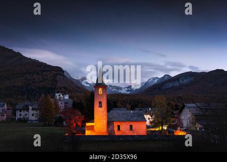 Vieux christianisme Église dans le village de Sils (près du Lac de Sils) dans les Alpes suisses. La lumière rouge sur la construction et les montagnes enneigées sur l'arrière-plan. La Suisse, Maloja, région de l'Haute Engadine. Photographie de paysage Banque D'Images