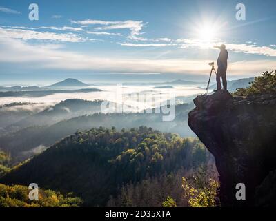 Le photographe prend des photos avec l'appareil photo dans les collines du matin. Photographe de paysages naturels avec équipement photo sur roc Banque D'Images