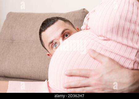 Mari écoutant le ventre de sa femme enceinte sur le canapé à la maison. Banque D'Images