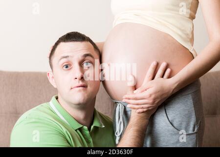 Jeune homme barbu mettant son oreille près de son abdomen enceinte et l'écoutant. Banque D'Images