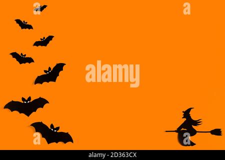 Silhouettes d'un troupeau de chauves-souris et d'une sorcière volant sur un balai en papier noir sur fond orange. Modèle de message d'accueil pour Halloween avec espace de copie Banque D'Images