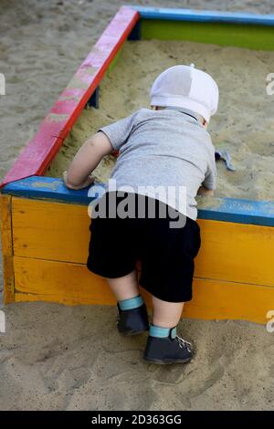 Enfant jouant sur le terrain de jeu dans la période chaude de l'année. L'enfant creusant dans le bac à sable des enfants. Vue arrière. Banque D'Images