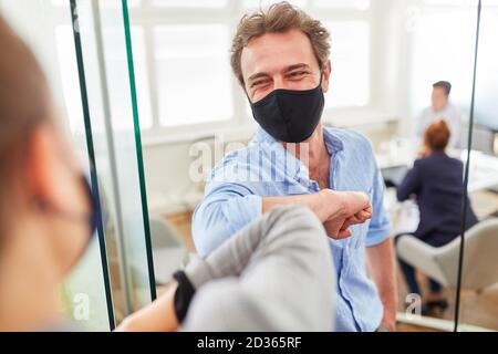 Deux collègues d'affaires avec des masques de tous les jours se saluent coudes au bureau Banque D'Images