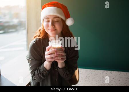 Modèle féminin en chapeau de noël tient une tasse avec le café à la main. Une jeune femme a fermé les yeux et souriait Banque D'Images