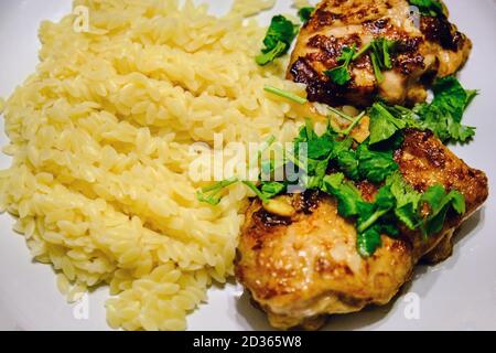 Pâtes Orzo au poulet grillé. Macaroni sous forme de riz à la viande et aux herbes. Pâtes sur une assiette de poulet frit saupoudrées de persil. Banque D'Images