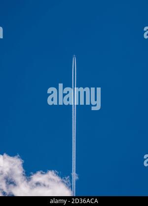 Avion dans le ciel bleu avec un sentier de condensation et un nuage dans le coin inférieur gauche Banque D'Images