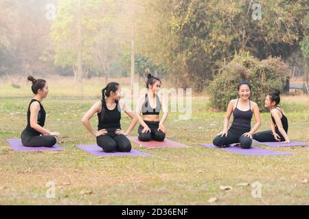 Groupe de femmes asiatiques ayant le repos après les pratiques de yoga. Femmes assises et parlant dans un parc extérieur. Banque D'Images