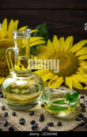 Huile de tournesol dans une bouteille et graines de tournesol près d'une fleur de tournesol fraîche sur fond de bois. Banque D'Images