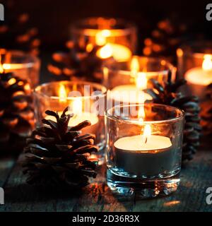 Composition de Noël ou du nouvel an avec bougies allumées en petits chandeliers en verre et cônes de pin, fond en bois vintage, soirée festive, selecti Banque D'Images