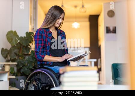 Femme en fauteuil roulant lisant un livre à la maison Banque D'Images