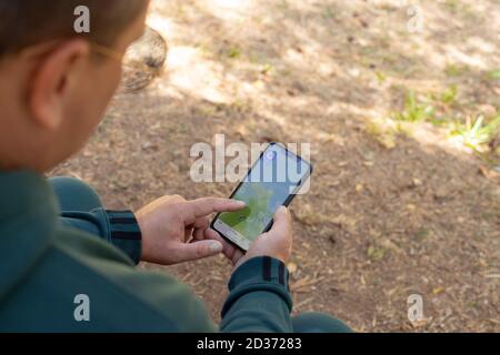 homme utilisant un smartphone avec une carte en ligne à la recherche de la bonne piste dans la forêt. Banque D'Images