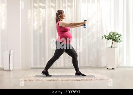 Prise de vue en profil pleine longueur d'une femme enceinte qui fait de l'exercice avec haltères bleues à la maison Banque D'Images