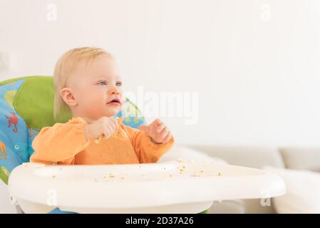 Portrait d'une adorable petite fille aux yeux bleus assis dans la chaise haute et déjeuner. Banque D'Images