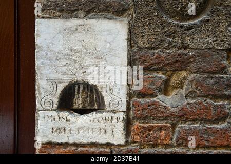 Gros plan d'un trou antique de charité en marbre gravé sur la façade d'un bâtiment médiéval en brique dans le centre historique de Sienne, Toscane, Italie Banque D'Images