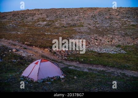 Paysage étonnant de crépuscule dans les montagnes avec tente sur le col dans la lumière violette. Tente près de la colline rocheuse dans la lumière lilas. Paysage de montagne avec c Banque D'Images