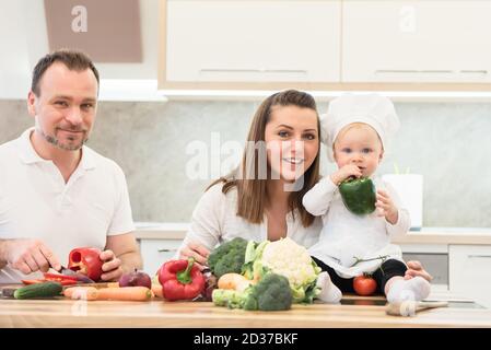 Heureux parents assis dans la cuisine et prépare pour la cuisine avec leur chef de fille de bébé. Banque D'Images