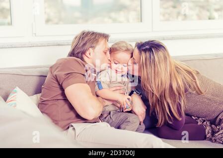 Portrait d'une famille heureuse assise sur le canapé et jouant. Les parents embrassaient leur bébé fils. Banque D'Images