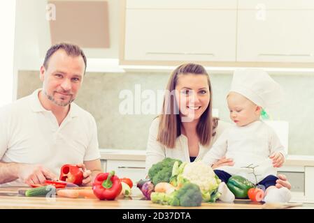 Heureux parents assis dans la cuisine et prépare pour la cuisine avec leur chef de fille de bébé. Banque D'Images