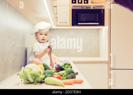 Bébé garçon assis parmi les légumes dans la cuisine et prépare pour cuisiner Banque D'Images