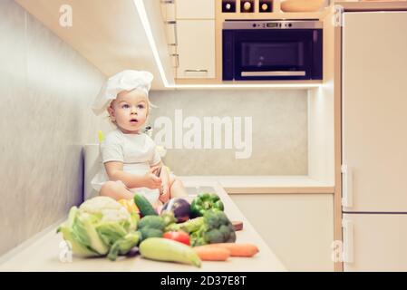 Bébé garçon assis parmi les légumes dans la cuisine et prépare pour cuisiner Banque D'Images