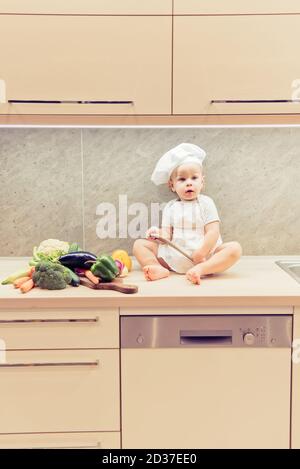 Bébé garçon assis parmi les légumes dans la cuisine et prépare pour cuisiner Banque D'Images