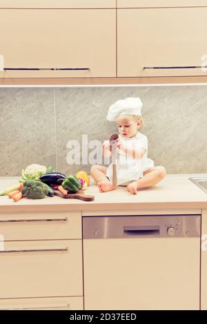 Bébé garçon assis parmi les légumes dans la cuisine et prépare pour cuisiner Banque D'Images