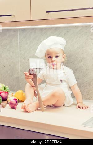 Bébé garçon assis parmi les légumes dans la cuisine et prépare pour cuisiner Banque D'Images