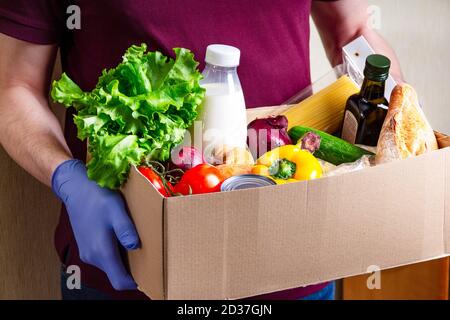 Portez un volontaire en portant des gants contenant des aliments dans une boîte en carton contenant divers aliments. Ouvrir la boîte en carton contenant de l'huile, des légumes, du lait, des conserves, des céréales Banque D'Images