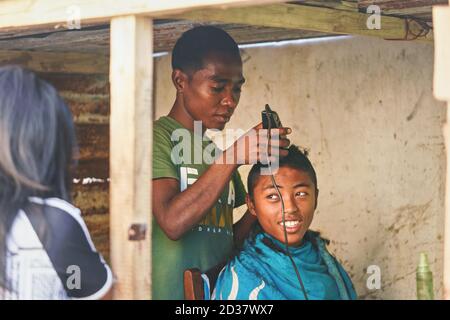 Ranohira, Madagascar - 29 avril 2019: Un garçon inconnu de la région obtient sa coupe de cheveux d'un ami à la boutique arrière de la salle faite à partir de planches en bois. Personnes dans ce p Banque D'Images