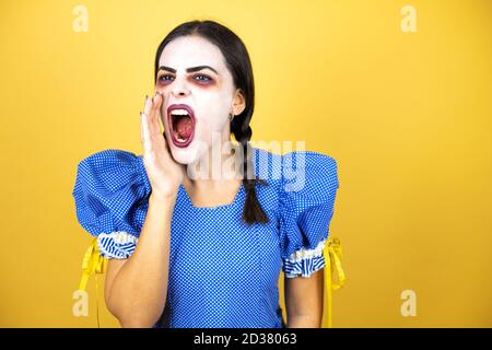 femme portant une poupée effrayante costume d'halloween sur fond jaune criant et criant fort à côté avec les mains sur la bouche Banque D'Images