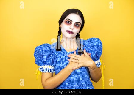 femme portant une poupée effrayante costume d'halloween sur fond jaune souriant avec ses mains sur sa poitrine et geste reconnaissant sur son visage. Banque D'Images