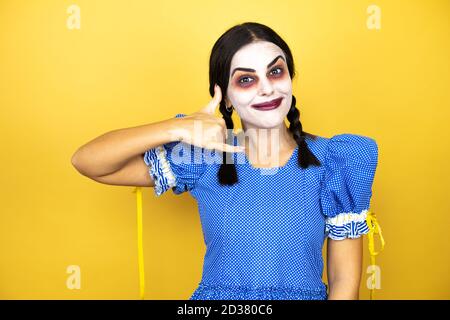 femme portant une poupée effrayante costume d'halloween sur fond jaune sourire faire un geste de téléphone avec la main et les doigts comme parler sur le téléphone Banque D'Images