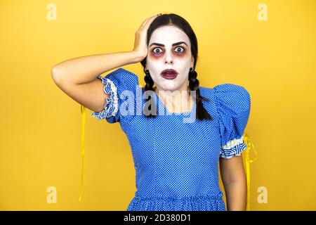 femme portant une poupée effrayante costume d'halloween sur fond jaune mettre une main sur sa tête en souriant comme elle l'avait fait quelque chose oublié Banque D'Images