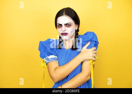 femme portant une poupée effrayante costume d'halloween sur fond jaune avec une douleur sur son épaule et une expression douloureuse Banque D'Images