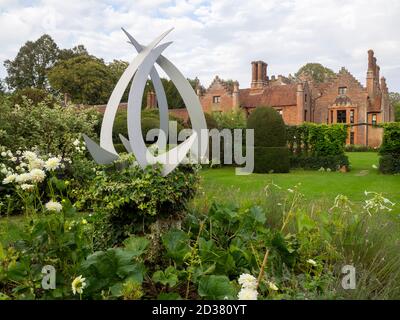 Chenies Manor jardin blanc en septembre. Vue sur le manoir Tudor ensoleillé avec topiaire d'arbre Yew et sculpture en acier blanc. Banque D'Images