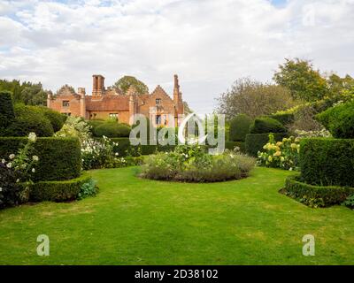 Chenies Manor jardin blanc en septembre. Vue sur le manoir Tudor ensoleillé avec topiaire d'arbre Yew et sculpture en acier blanc. Banque D'Images