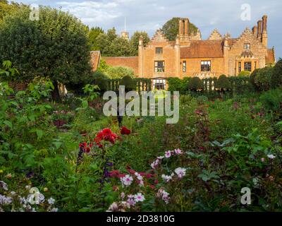 Chenies Manor House au soleil ; le jardin en contrebas en septembre avec la sculpture d'Alan Bigg sur « le plongeur », qui se retrouve à travers l'exposition dynamique des dahlia. Banque D'Images