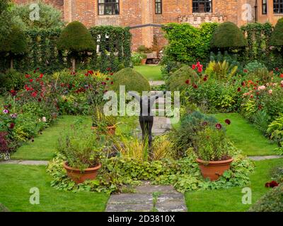 Chenies Manor House au soleil ; le jardin en contrebas en septembre avec la sculpture d'Alan Bigg sur « le plongeur », qui se retrouve à travers l'exposition dynamique des dahlia. Banque D'Images