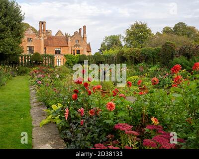 Chenies Manor House au soleil ; le jardin en contrebas en septembre avec la sculpture d'Alan Bigg sur « le plongeur », qui se retrouve à travers l'exposition dynamique des dahlia. Banque D'Images