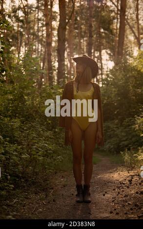 Hippie femme en maillot de bain et chapeau de cow-boy dans la forêt au coucher du soleil. Banque D'Images