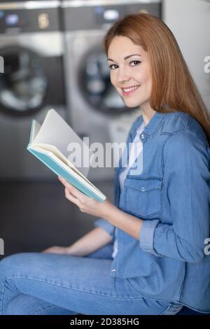 photo d'une jeune femme lisant un livre dans une laverie automatique Banque D'Images