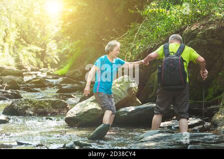 Couple asiatique senior traversant une petite rivière dans un parc naturel Banque D'Images