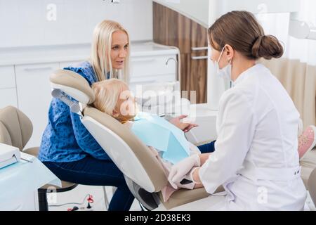 Une femme pédiatrique spécialiste dentaire qui passe sur les résultats de l'examen oral de la fille avec sa mère. Bureau de dentiste. Banque D'Images