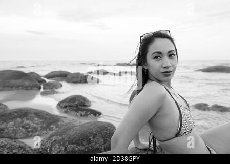 Belle jeune femme asiatique alors que la pensée assis sur les rochers de la plage publique de Hua Hin Thaïlande Banque D'Images