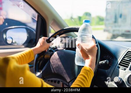 Femme asiatique tenant une bouteille d'eau pour boire tout en conduisant la voiture le matin pendant qu'elle va travailler sur la route, le transport et le véhicule con Banque D'Images