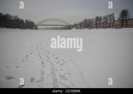 Empreintes de pas dans la neige sur une rivière gelée menant loin et vers un pont lointain dans une ville russe éloignée Banque D'Images