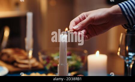 Une jeune femme qui éclaire la bougie attend son mari pour un dîner romantique. Femme préparant un repas de fête avec de la nourriture pour la fête d'anniversaire, date romantique, assis près de la table dans la cuisine. Banque D'Images