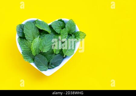 Feuilles de menthe fraîche dans un bol en forme de coeur sur fond de jaune. Vue de dessus Banque D'Images